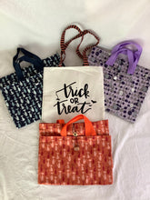 Load image into Gallery viewer, A collection of four tote bags with different patterns and colors, including black and white, orange, navy, and purple, with 'TRICK OR TREAT' text on a white bag.