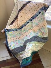 Load image into Gallery viewer, A multicolored striped quilt with a flannel back, draped over a chair in a home environment.