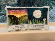 Load image into Gallery viewer, Soft books with illustrations of desert scenes and moonlit nights, placed on a surface with a blurred natural background.