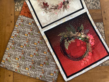 Load image into Gallery viewer, A reversible table runner with one side featuring a Christmas fabric pattern with red and white colors and a wreath design, and the other side with an autumn leaf pattern in shades of brown and red.