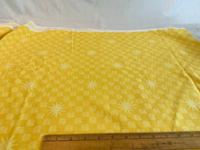 Load image into Gallery viewer, Yellow fabric with a repeating white starburst and small square pattern, laid flat with a wooden ruler along the bottom edge to show scale.

