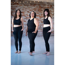Load image into Gallery viewer, Three women standing barefoot in a studio with a brick wall background, wearing matching black activewear sets consisting of sleeveless crop tops and high-waisted leggings.
