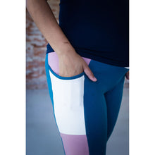 Load image into Gallery viewer, Close-up of a person wearing color-blocked leggings with a pocket, showing a navy top, a hand in the pocket, and panels of navy, white, teal, and dusty pink.
